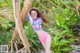 A woman in a pink bikini leaning against a tree.