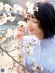 A woman in a blue dress standing next to a tree with white flowers.