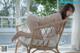 A woman in a white bikini sitting on a wicker chair.