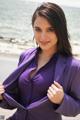 A woman in a purple shirt is posing on the beach.