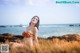 A woman in a bikini sitting on a rock by the ocean.